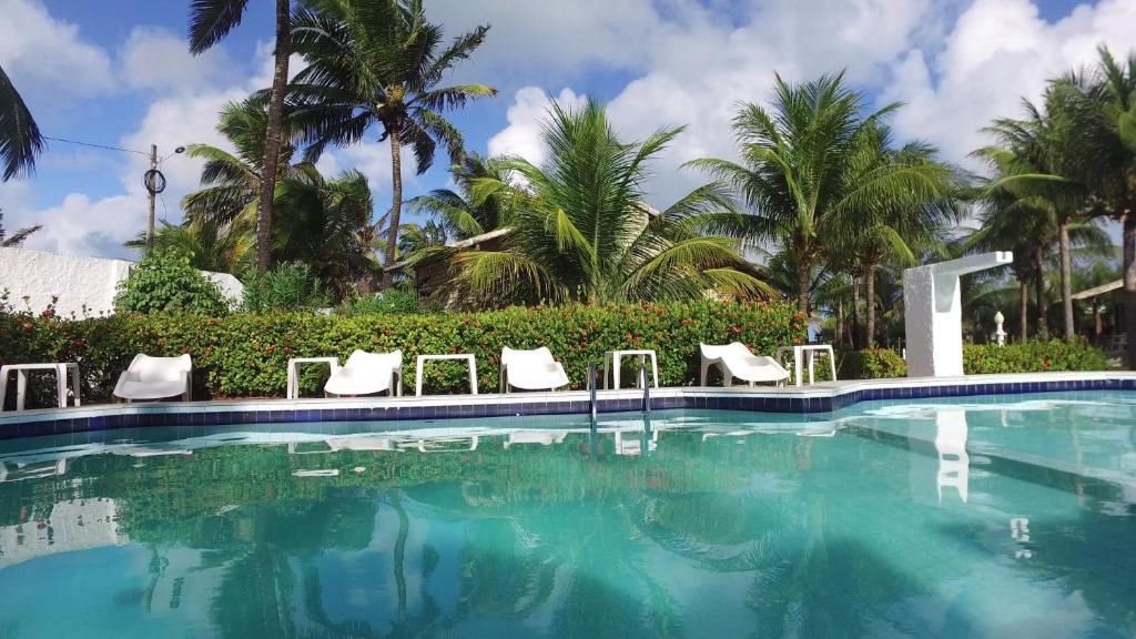 a swimming pool with white chairs and palm trees at Pousada Caribe Sul in Barra do Cunhau