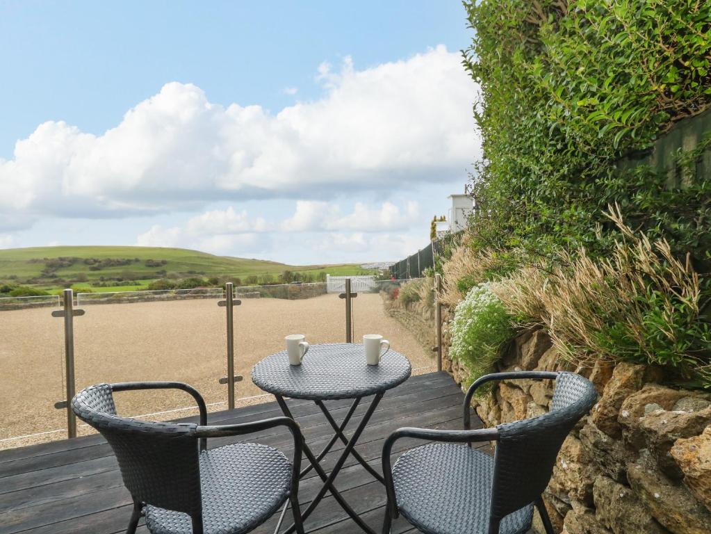 a table and chairs on a wooden deck with a view of the ocean at Burton Bay in Burton Bradstock
