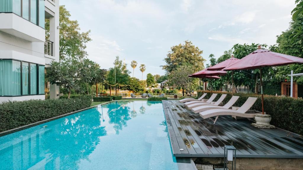 A long pool runs beside a timber deck lined with loungers and burgundy umbrellas.