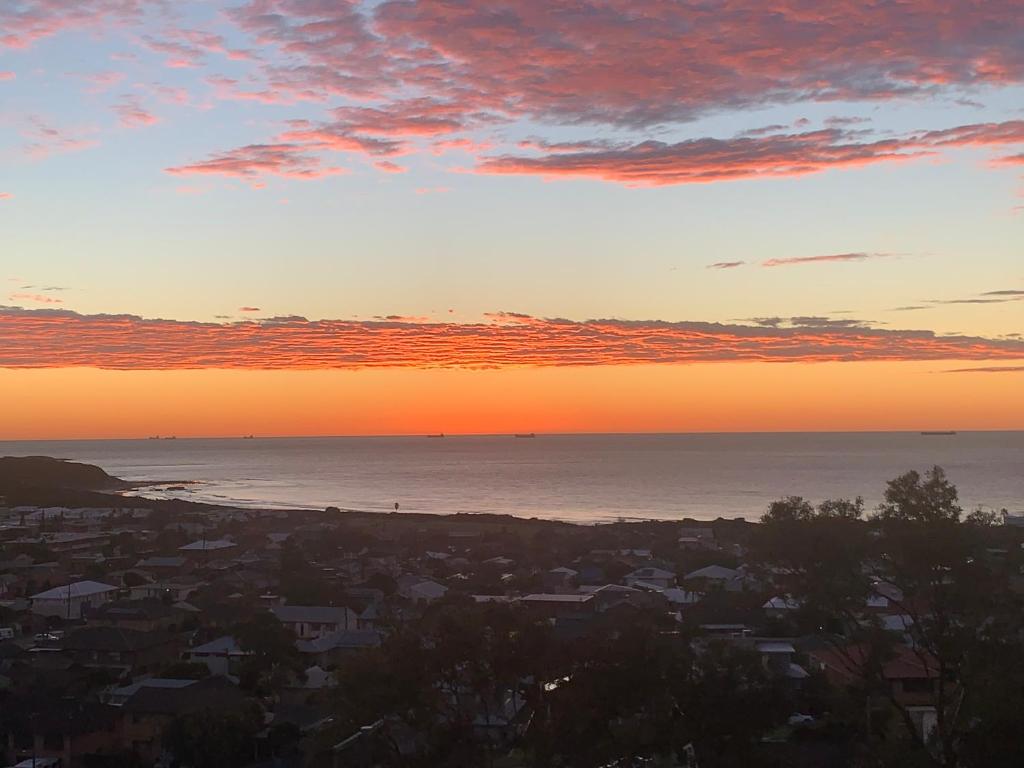 a sunset over the ocean and a city at Panoramata @ Caves Beach in Caves Beach