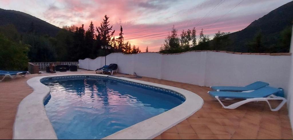 una piscina con 2 sillas y una puesta de sol en Casa Benamahoma, en Benamahoma
