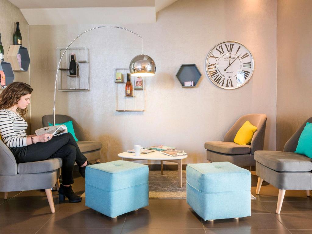 a woman sitting in a waiting room with a clock at Novotel Suites Reims Centre in Reims