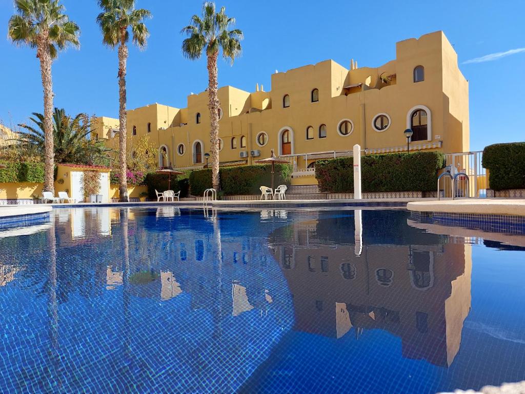 een zwembad met palmbomen en een gebouw bij Bungalow Alkabir Playa in El Campello