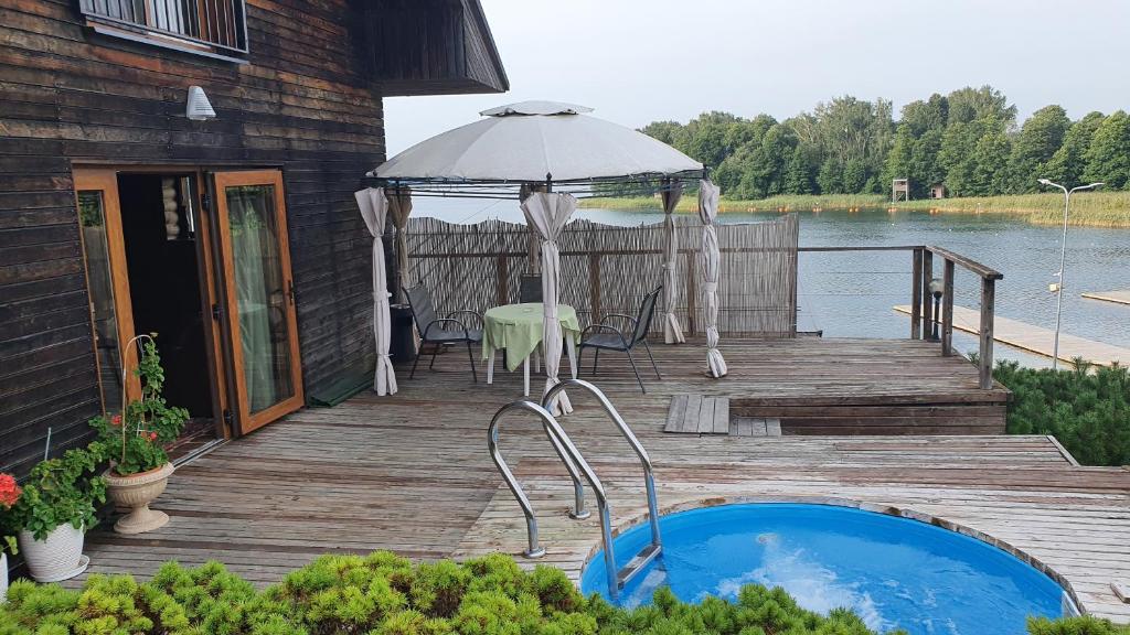 una terraza de madera con bañera de hidromasaje y sombrilla en Prie Galvės, en Trakai