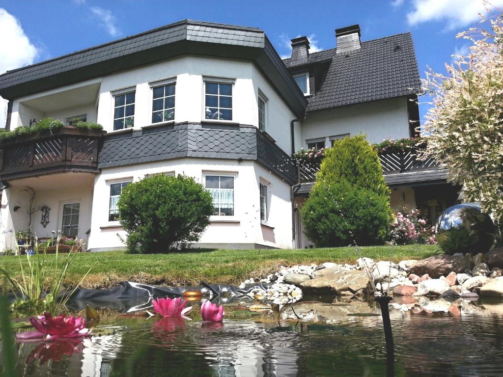 uma casa com um lago em frente com flores cor-de-rosa em Ferienwohnungen Luge - Winterberg em Winterberg