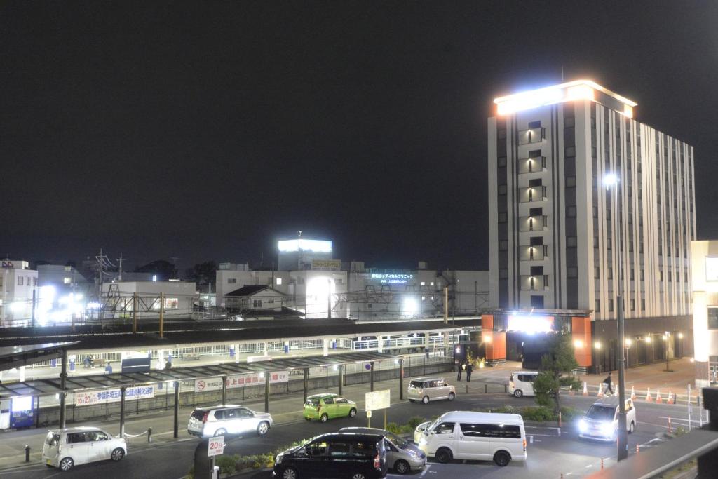 um parque de estacionamento com carros estacionados em frente a um edifício em APA Hotel Saitama Higashimatsuyama Ekimae em Matsuyama