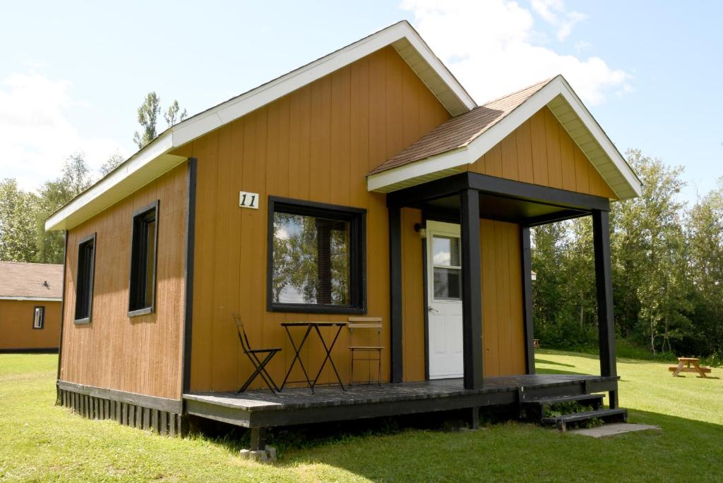 a small yellow house with a porch on the grass at Chalets du Lac Matapédia in Val-Brillant