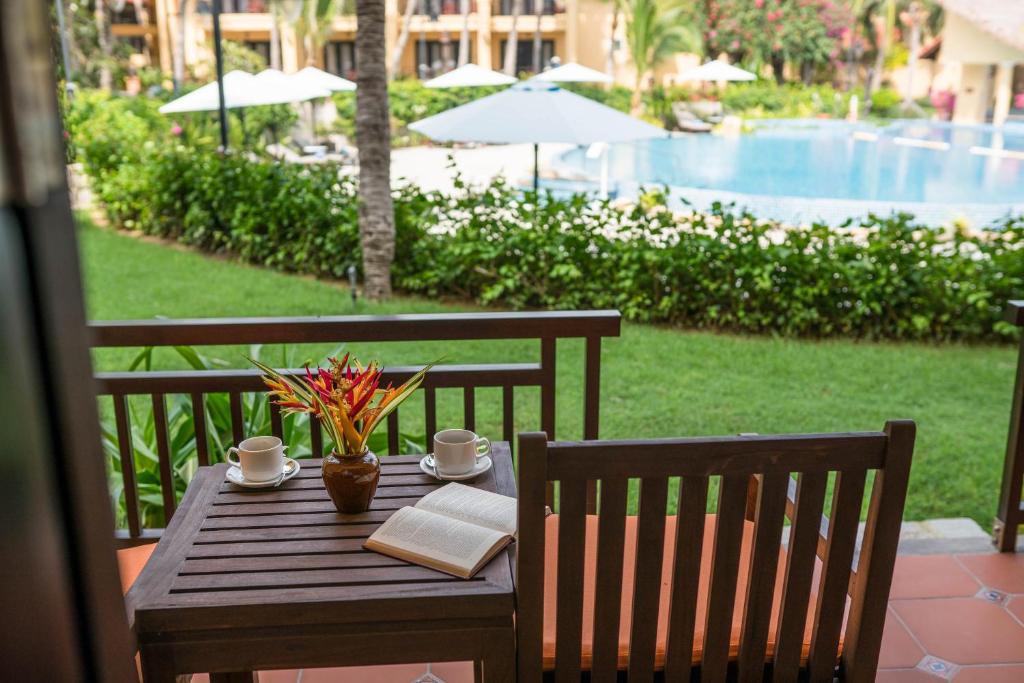 a wooden table with a book and coffee cups on a patio at Pandanus Resort in Mui Ne