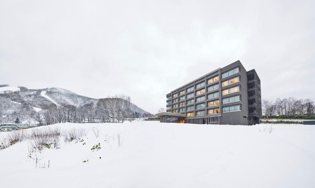 um edifício na neve em frente a um campo em Hinode Hills Niseko Village - Small Luxury Hotels of The World em Niseko