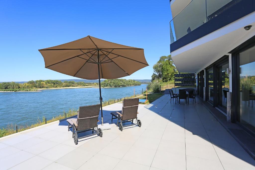 a patio with chairs and an umbrella next to the water at Rhein Lounge in Urmitz