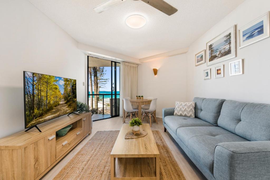 sala de estar con sofá azul y TV de pantalla plana en Coolum Beachside Apartments, en Coolum Beach