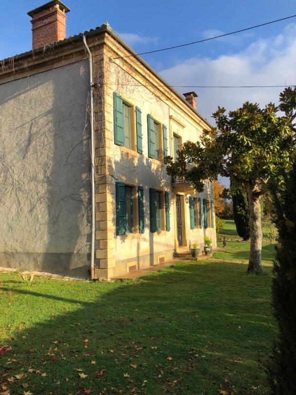 a brick building with green windows and a tree at la maison d'Obinat in Auzas