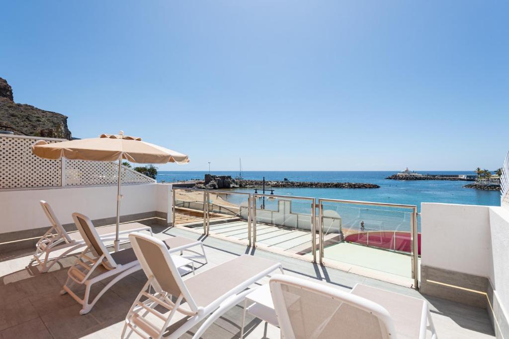 a balcony with chairs and an umbrella and the ocean at BLUE SEA I in Puerto de Mogán