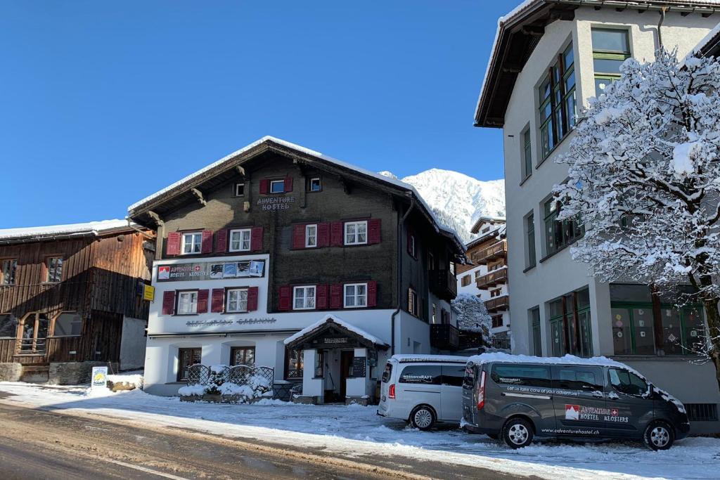 un bâtiment avec deux voitures garées devant lui dans l'établissement Adventure Hostel, à Klosters