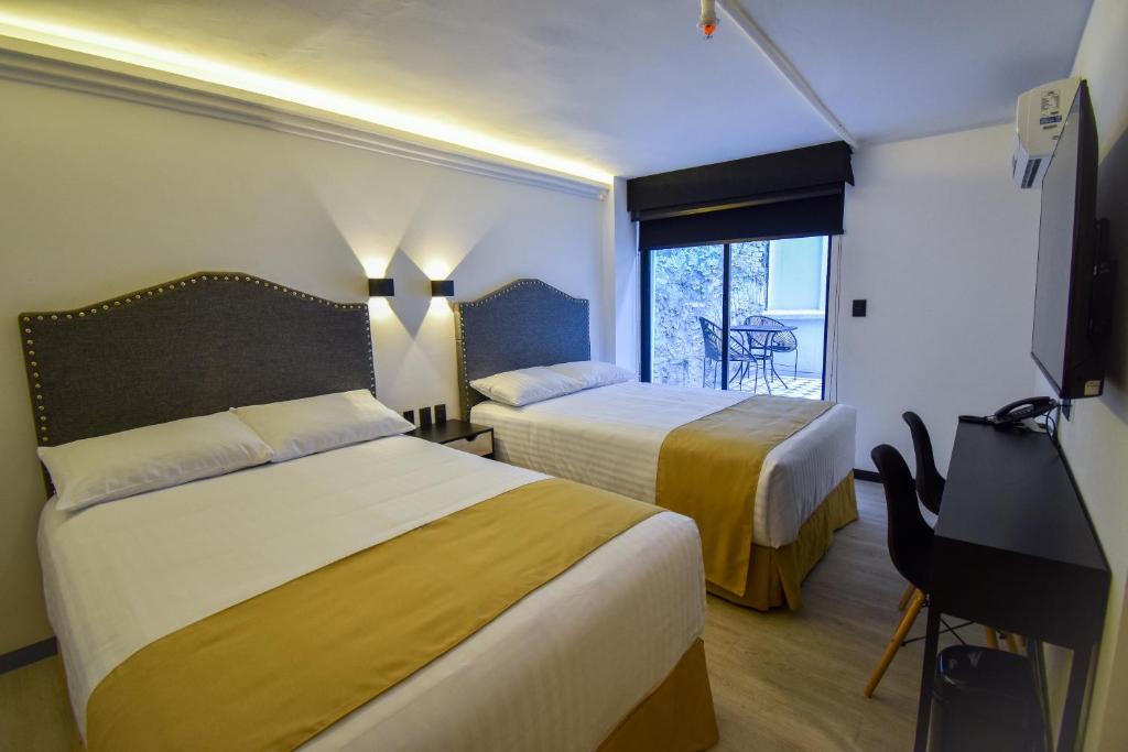 a hotel room with two beds and a desk and a window at Hotel Tamara in Puebla