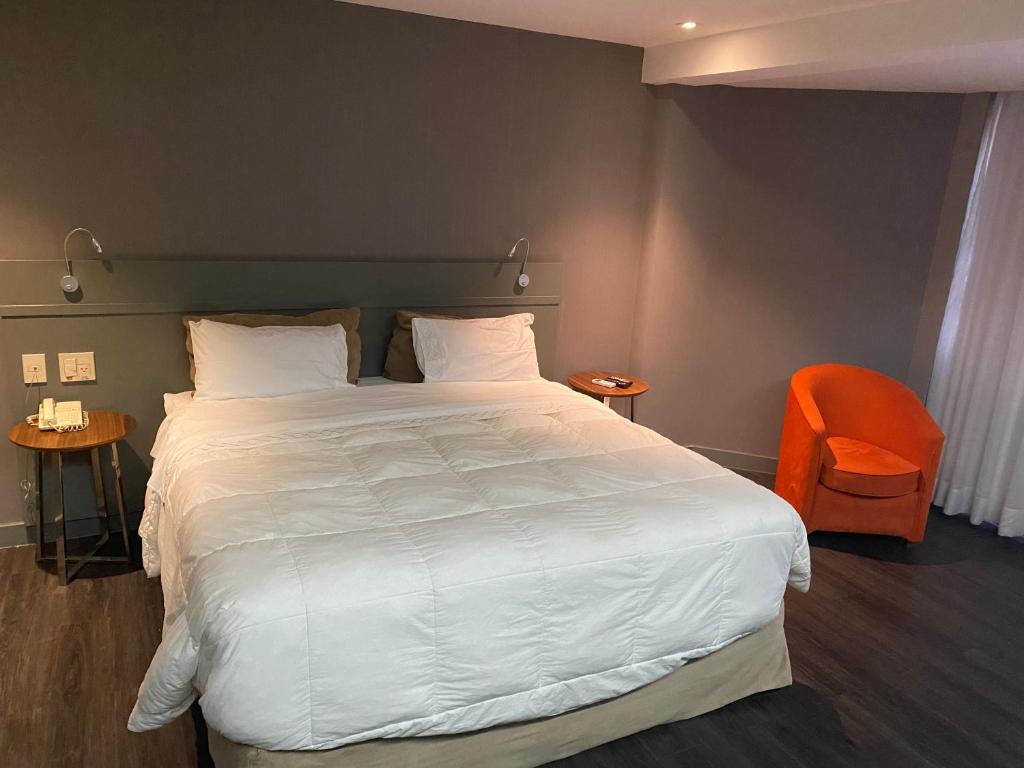 ein Schlafzimmer mit einem großen weißen Bett und einem orangenen Stuhl in der Unterkunft Grand Mercure Brasília - Ap Particular 112 in Brasilia