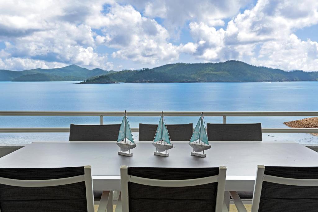 a white table with chairs and a view of the water at Frangipani Beachfront Lodge 202 on Hamilton Island by HamoRent in Hamilton Island