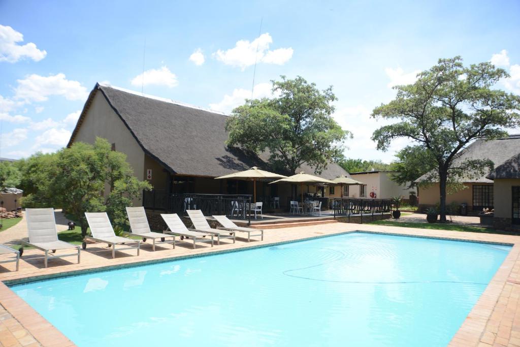 a swimming pool with lounge chairs and a building at Ukutula Lion Lodge in Brits