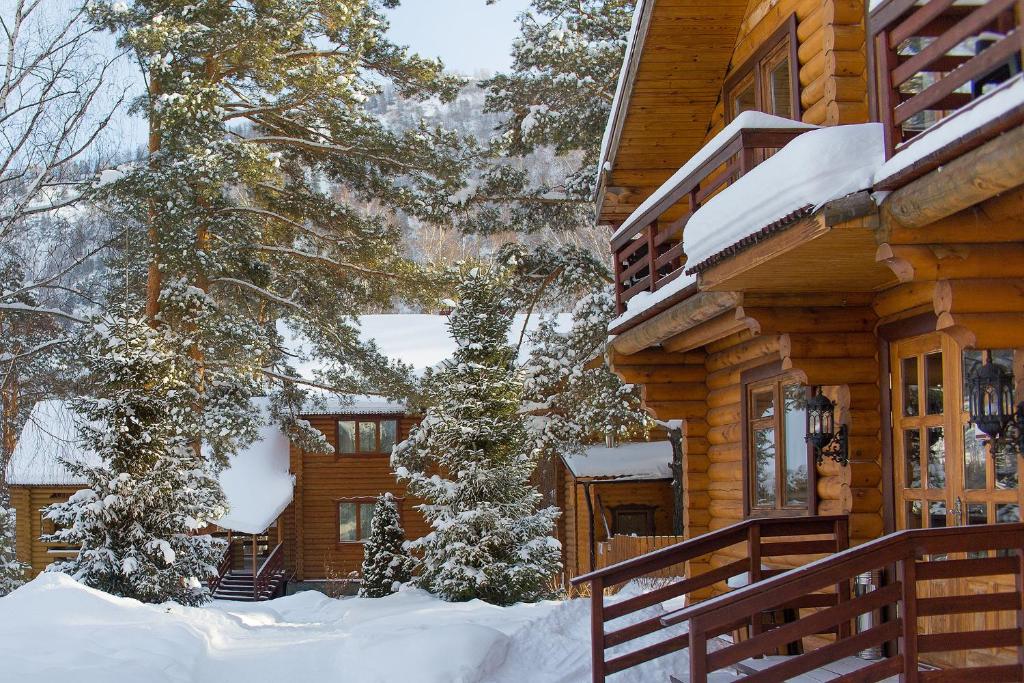a log cabin in the snow next to a tree at Hotel Usadba Sarzhevskikh on Biryuzovaya ulitsa 1 in Bol'shoy Kaim