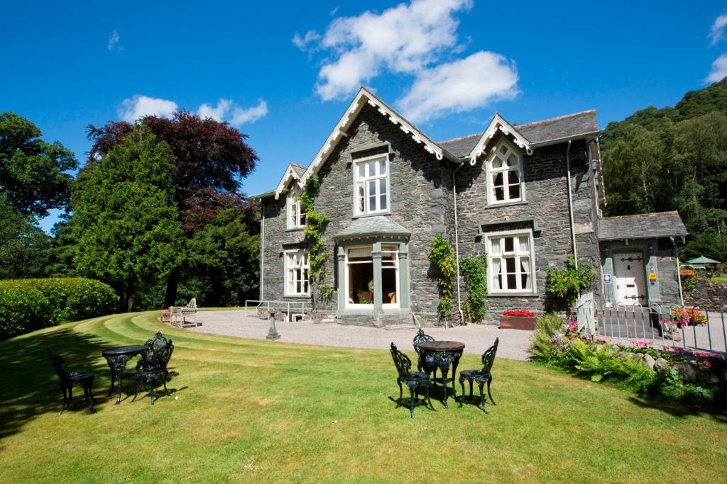 une grande maison en pierre avec des chaises dans la cour dans l'établissement Hazel Bank Country House Borrowdale Valley, à Rosthwaite