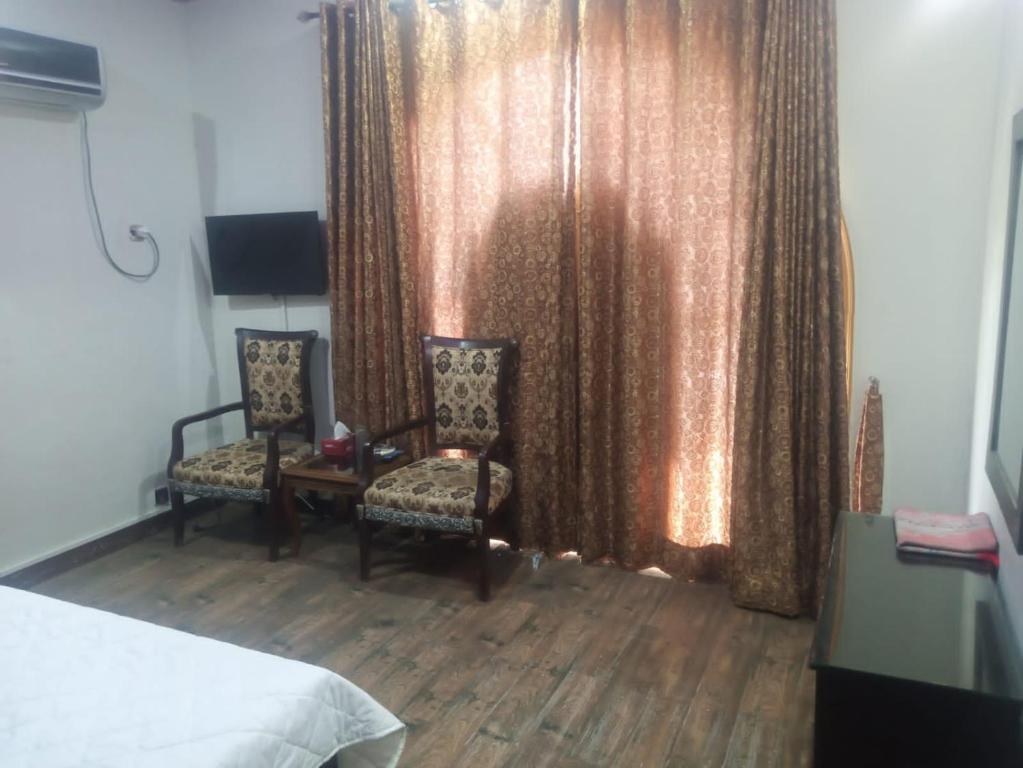 ein Schlafzimmer mit 2 Stühlen und ein Fenster mit Vorhängen in der Unterkunft Four Season Guest House in Islamabad