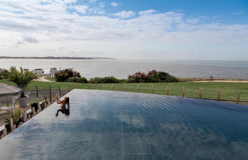 a man standing in a swimming pool overlooking the water at Thalazur Royan - Hôtel & Spa in Royan