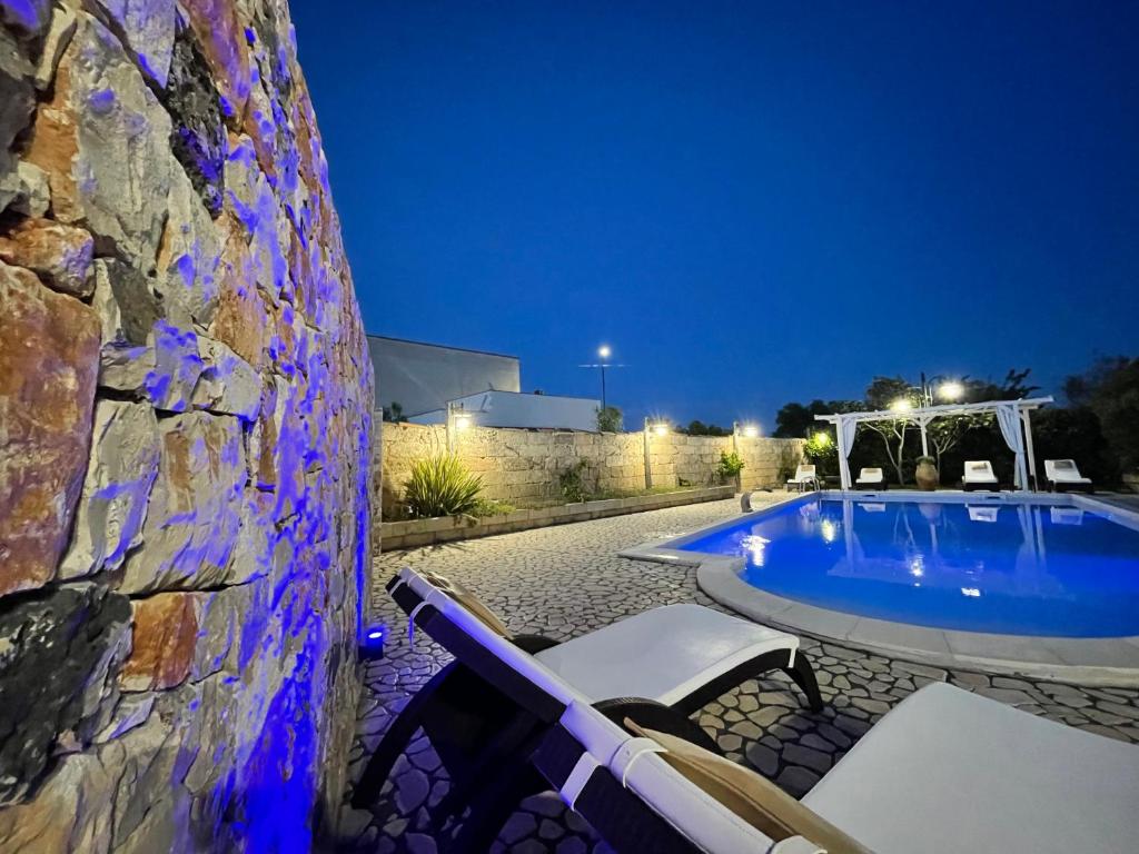 uma piscina com cadeiras e uma parede de pedra à noite em Villa B&B Antiche Macine del Salento - nel cuore del Salento em Salve