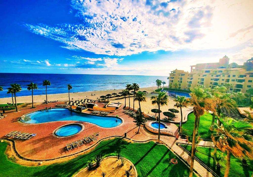 a resort with a pool and a beach with palm trees at Right on the Beach! Ocean Front 2 Story Penthouse in Puerto Peñasco