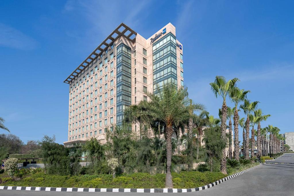 a tall building with palm trees in front of a street at Radisson Blu Hotel Amritsar in Amritsar
