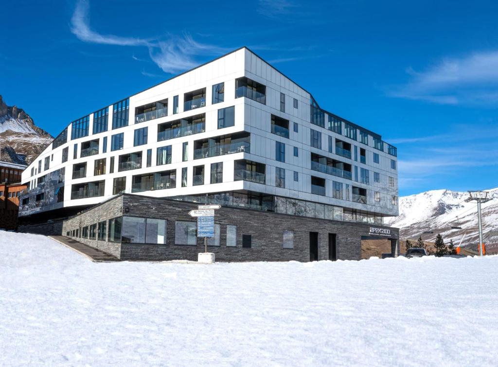 un gran edificio en la nieve con montañas en el fondo en Hôtel VoulezVous by Les Etincelles, en Tignes