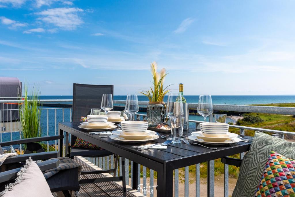 a table with glasses and plates on a balcony with the ocean at Sounds of the Sea in Olpenitz