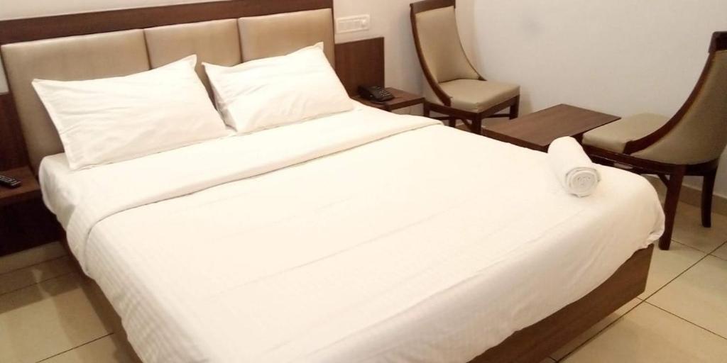 a white bed in a hotel room with two chairs at Vels Residency in Puducherry
