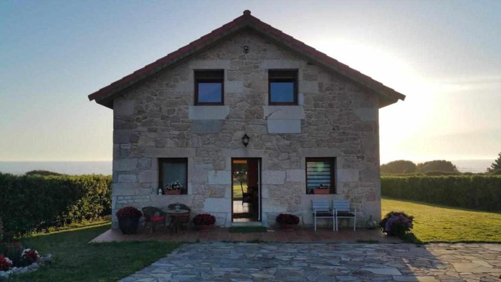 een stenen huis met tafels en stoelen ervoor bij Cubelas Porto do Son in Porto do Son