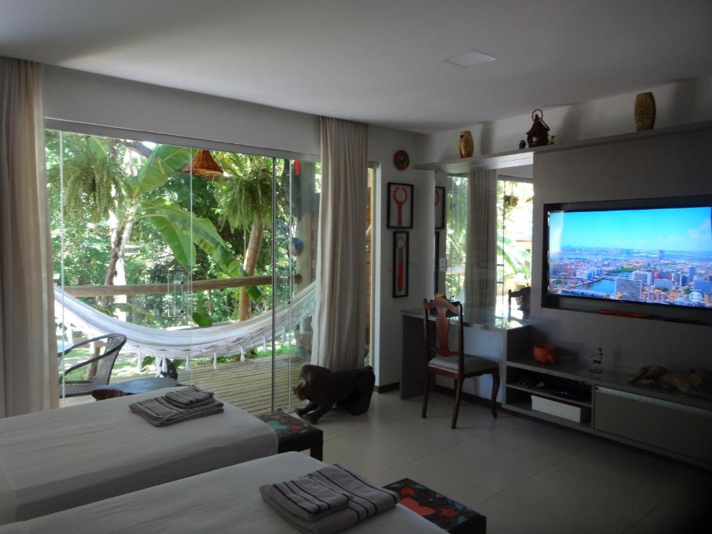 a bedroom with two beds and a large window with a television at Bangalô no alto da colina no Villas do Pratagy - Maceió in Maceió