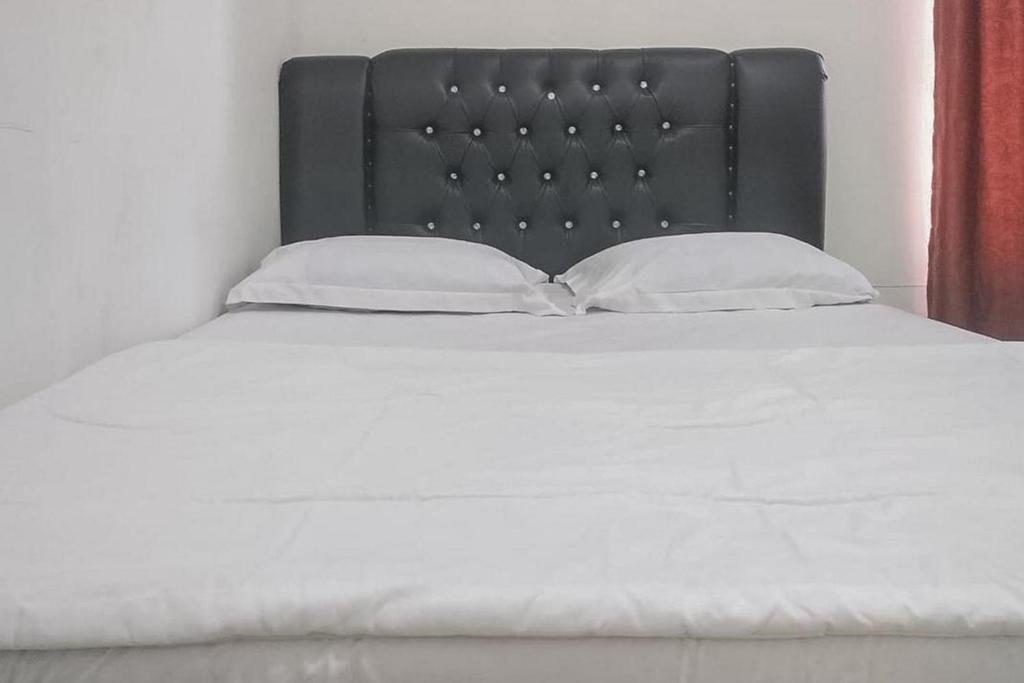 uma cama com uma cabeceira preta e duas almofadas brancas em Nayla Homestay Jambi Mitra RedDoorz em Kayu Aro