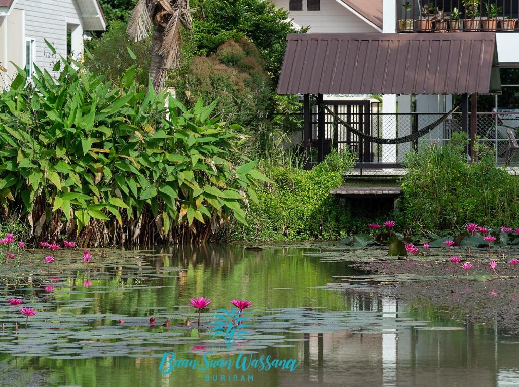 un étang en face d'une maison avec des fleurs roses dans l'établissement Baan Suan Wassana, à Buriram
