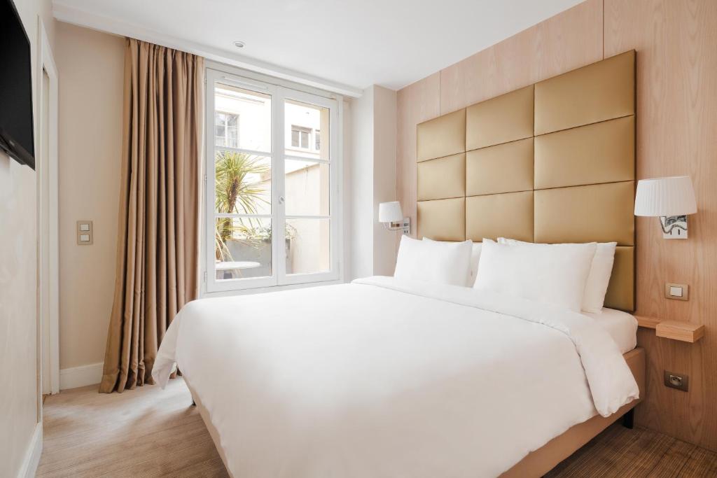 duże białe łóżko w pokoju hotelowym z oknem w obiekcie Sonder L'Edmond Parc Monceau w Paryżu
