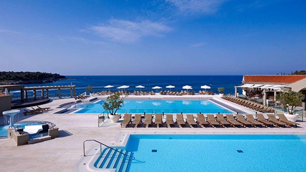 einen Pool mit Stühlen und das Meer im Hintergrund in der Unterkunft Park Plaza Verudela Pula in Pula