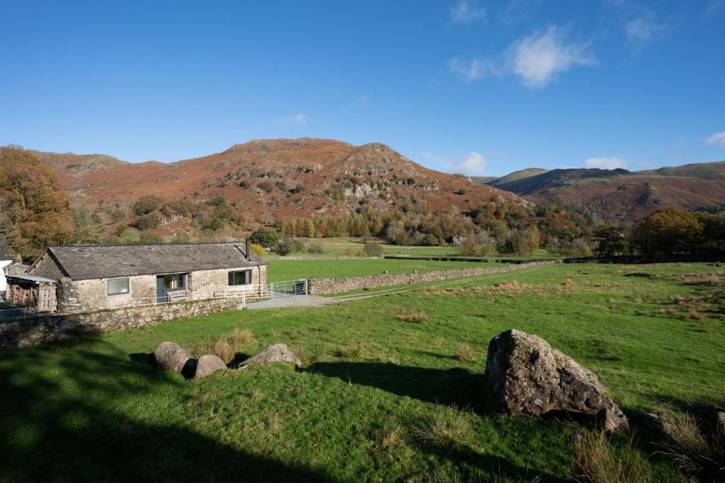 ein Steinhaus auf einem Feld mit Bergen im Hintergrund in der Unterkunft Grasmere Cottage with Stunnng Views by LetMeStay in Ambleside