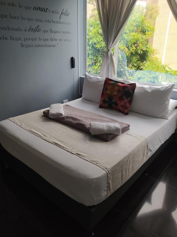 Una cama con almohadas blancas y una ventana en una habitación. en Hotel Aura Medellin en Medellín