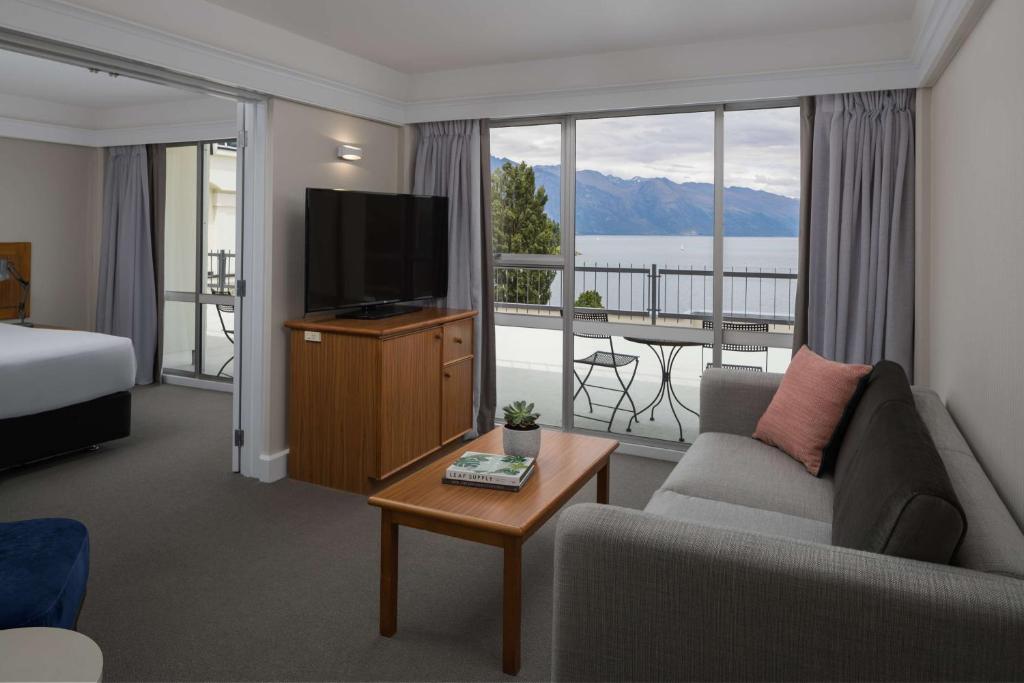 a hotel room with a couch and a television and a balcony at Rydges Lakeland Resort Queenstown in Queenstown