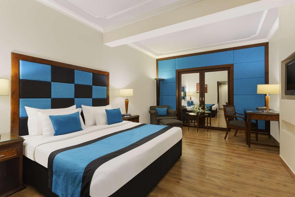 ein Hotelzimmer mit einem großen Bett und einem Schreibtisch in der Unterkunft Park Plaza, Ludhiana in Ludhiana