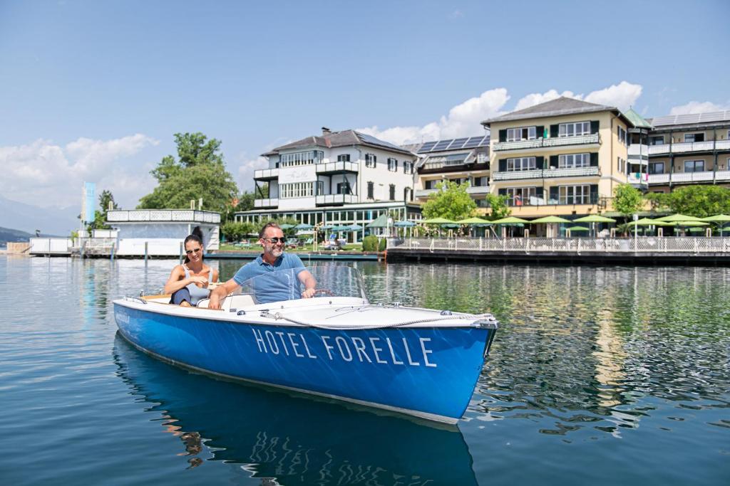 Un uomo e una donna seduti su una barca blu sull'acqua di SEEGLÜCK Hotel Forelle Superior a Millstatt