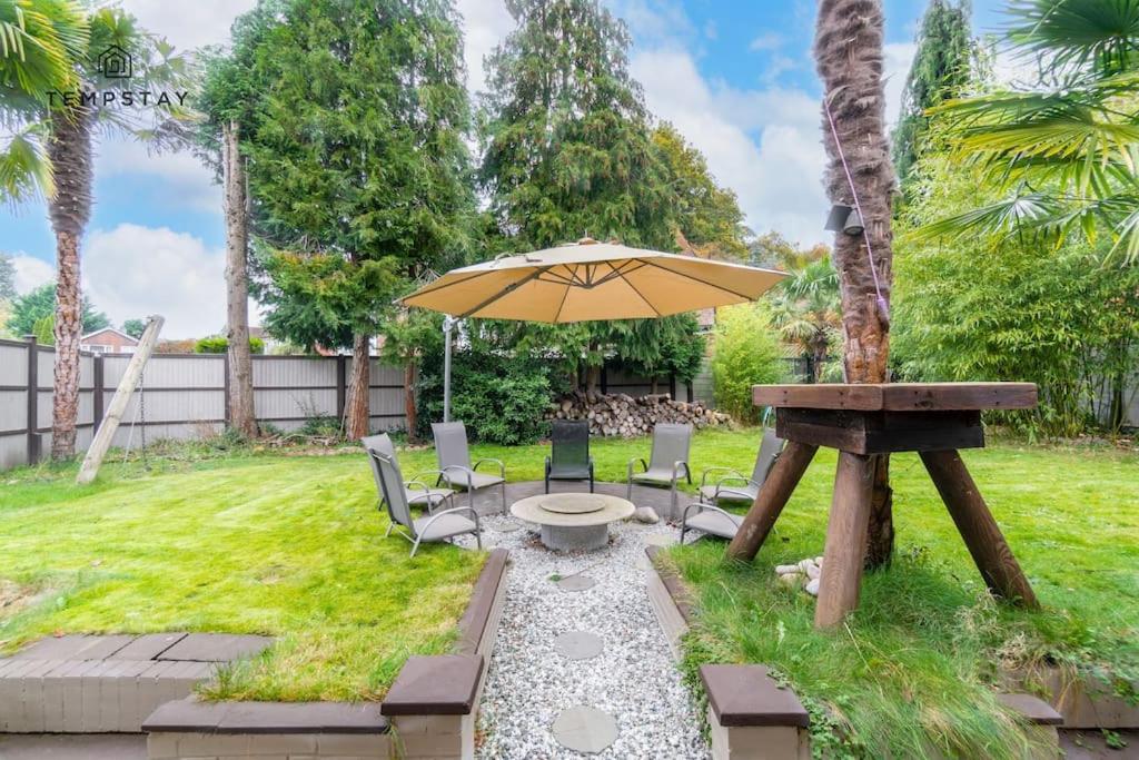 a patio with an umbrella and chairs and a table at LARGE COSY HOME @ WENTWORTH, SUNNINGDALE, ASCOT in Sunningdale