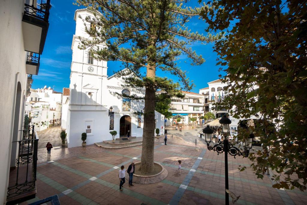 una plaza de la ciudad con un árbol y una iglesia en BALCON DE EUROPA 4 MENYBER en Nerja