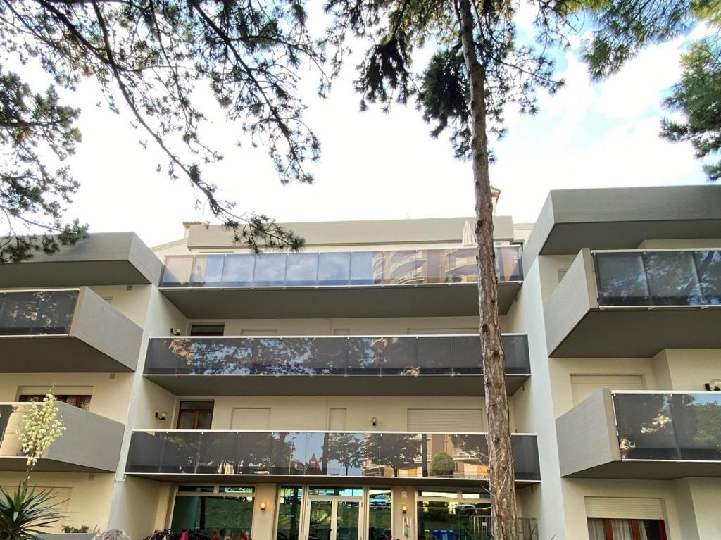 un edificio de apartamentos con balcones y árboles en Appartamenti Vacanza Albatros, en Lignano Sabbiadoro