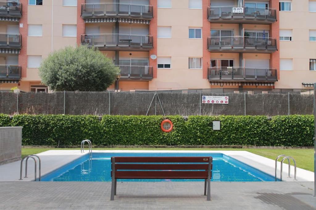 un banco junto a una piscina con un edificio en Bonito apartamento a 250m del mar en Lloret de Mar