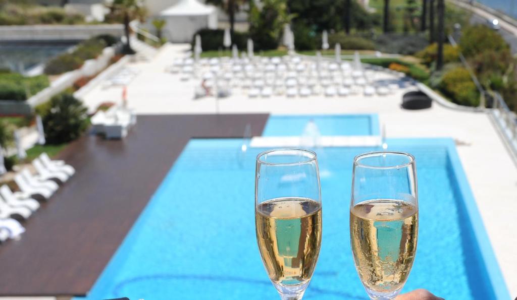 two champagne glasses sitting on a table next to a swimming pool at Hotel Cascais Miragem Health & Spa in Cascais