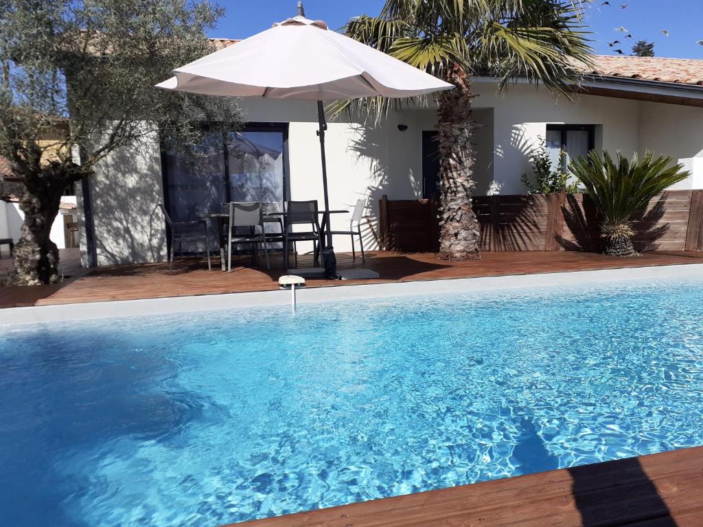 a swimming pool with an umbrella and a house at ViLLA NEUVE 115m2 ,TOUT CONFORT AVEC PiSCiNE Chauffée-JARDiNET BASSiN ARCACHON in Gujan-Mestras