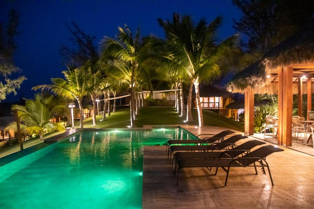 a pool with lounge chairs and palm trees at night at Collina Beach in Amontada